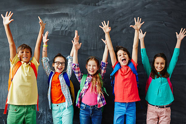 6th grade students in front of a chalkboard with hands up