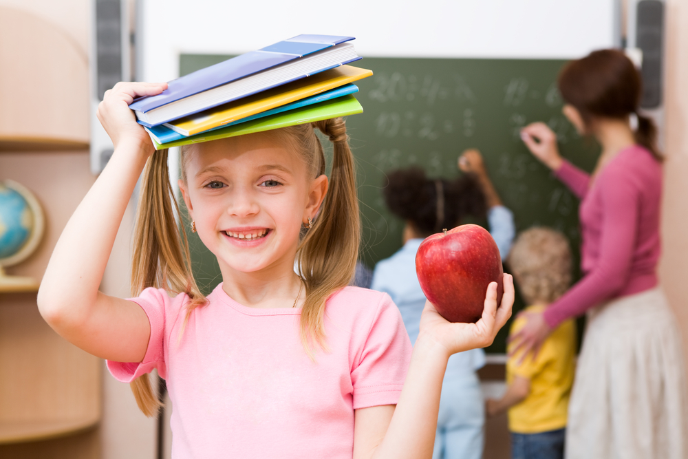 A girl student holding books on her head with an apple in the other hand